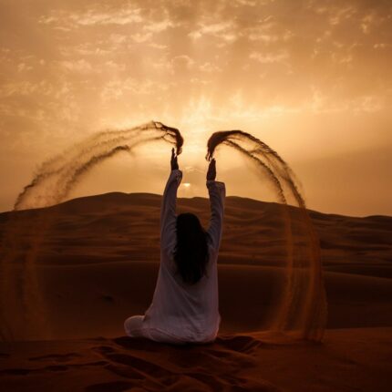 woman sitting on desert while playing sand during golden hour